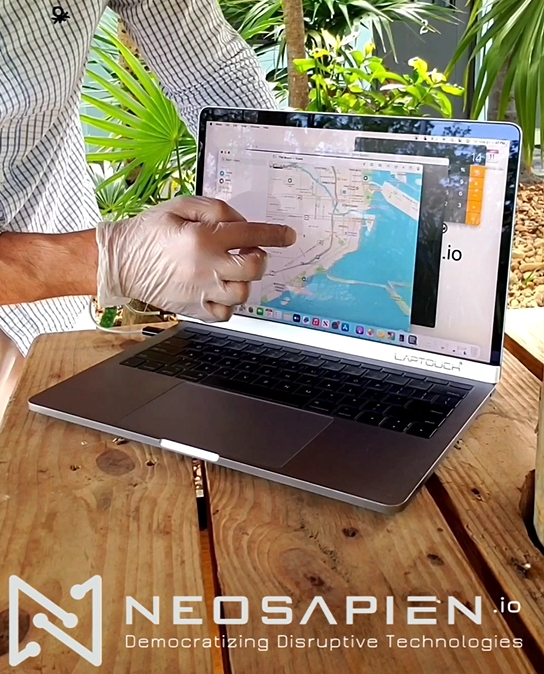 Even works with gloves! Person using a laptop with a map on the screen, wearing gloves, on a wooden table with plants in the background. NEOSAPIEN.