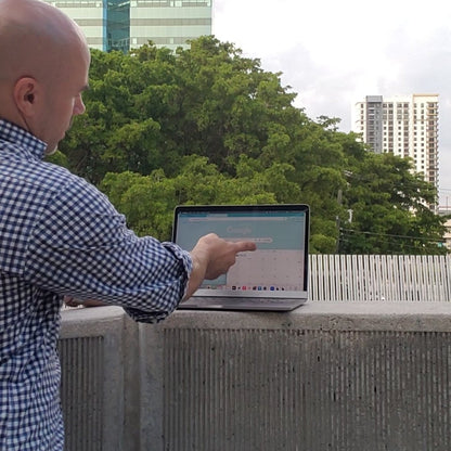 Man using a laptop outdoors with trees and buildings in the background